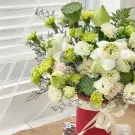 A red box overflowing with white lotuses, green carnations, lisianthus, and lotus seed pods.