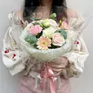 Woman holding a pink and white flower bouquet wrapped in clear plastic with a pink bow.