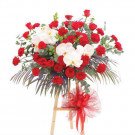Floral arrangement with red roses, white orchids, and greenery on a wooden stand with a red bow.