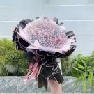 A person holds a large bouquet of rainbow-colored baby's breath flowers wrapped in black and pink paper.