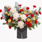 A large floral arrangement in a black box with white peonies, red and orange roses, and greenery.