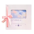 White notebook with pink ribbon, featuring a sky photo and "Just between us" text.