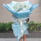 A large bouquet of blue hydrangeas and white baby's breath wrapped in blue and white paper.