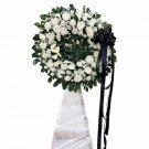 A white floral wreath with a black bow on a white stand.
