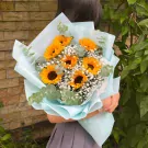 Bouquet of sunflowers and baby's breath wrapped in light blue paper.