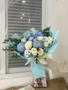 Bouquet of blue chrysanthemums, white roses, and daisies wrapped in light blue paper.