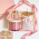 Pink gift box with candle, diffuser, and fabric pouch, adorned with ribbon and flowers.