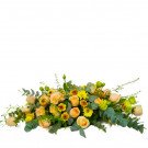 A table arrangement of peach and yellow roses, sunflowers, and greenery.