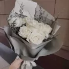 Bouquet of white roses wrapped in grey paper with a white envelope and ribbon.