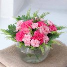 A pink carnation and rose floral arrangement in a clear glass bowl.