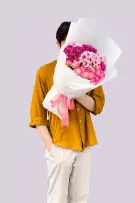 Person holding a pink and purple floral bouquet with white paper wrapping and pink ribbon.