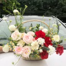 Flower basket with pink and red roses, white carnations, and daisies on a car hood.
