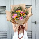Bouquet of sunflowers and purple roses wrapped in brown paper, tied with a brown ribbon.