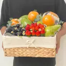 Fruit basket with oranges, pears, strawberries, grapes, and mangoes, decorated with flowers and leaves.