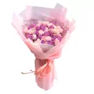 A bouquet of pink and purple roses wrapped in pink paper with a pink ribbon.