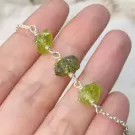 A silver bracelet with raw, green stones on a hand.