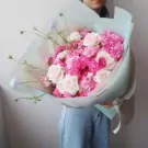 A lush bouquet of pink roses and carnations with delicate purple flowers, wrapped in pale blue paper.