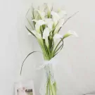Bouquet of white calla lilies tied with white lace ribbon, with a book in the foreground.