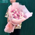 Man holding a large bouquet of pink and white roses wrapped in pale pink paper.