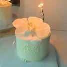 Mini cake with white orchid, lit candle, and "Happy Birthday" inscription.