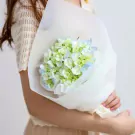 Woman holding a bouquet of blue and green hydrangeas wrapped in white paper.