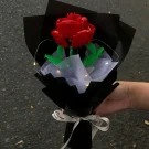 Red Lego rose bouquet wrapped in black paper with fairy lights and a white ribbon, held by a hand.
