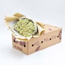 A bouquet of yellow tana daisies in a white woven holder, partially wrapped in brown paper, sits on an open cardboard box.