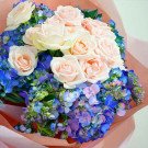 Bouquet of pink roses and blue hydrangeas in pink wrapping paper.