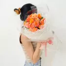 Woman holding a bouquet of orange and pink roses wrapped in clear plastic with a pink ribbon.