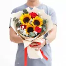 Man holding a bouquet of sunflowers and red roses with baby's breath and greenery.