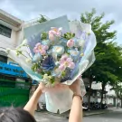A bouquet of pastel pink and blue roses and tulips, with a succulent and delicate white flowers.