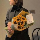 Woman holding a bouquet of sunflowers and greenery with a letter attached.