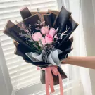 Pink roses and eucalyptus bouquet wrapped in black and brown paper, tied with a pink ribbon.