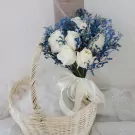White roses with blue accents in a basket, tied with a white ribbon.