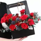 A black basket overflowing with red roses, carnations, and thistles.