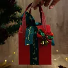 Red gift bag with green ribbon, Christmas bells, and pine.