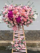 Pink and purple floral arrangement on a wooden easel, featuring roses, orchids, and other blooms.