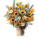Basket of sunflowers, gerbera daisies, and eucalyptus in a wooden box with a brown ribbon.