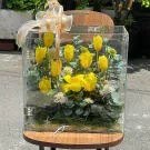 Yellow tulips and greenery in a clear acrylic box with a ribbon bow.
