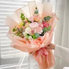 A bouquet of pink and white flowers wrapped in peach paper with a pink ribbon.