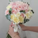 A bridal bouquet of pink and white roses and yellow carnations, tied with a white ribbon.