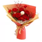 Red roses and carnations in a bouquet with white accent flowers, wrapped in red and yellow paper.