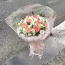 Pink and white roses and other flowers in a bouquet with a pink ribbon.