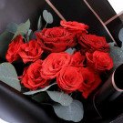 Bouquet of vibrant red roses with water droplets, accented with green eucalyptus leaves.