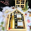 Christmas gift box with champagne, cookies, granola, and festive decorations.