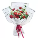 Bouquet of red ranunculus and white tana flowers, wrapped in white paper with a burgundy ribbon.