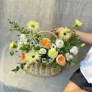 Basket of yellow and orange roses, carnations, and daisies with greenery.