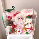 Clear box filled with a plush bunny, teddy bear, flowers, and Christmas decor.