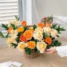 Basket of orange and cream roses with green foliage on a burlap cloth.
