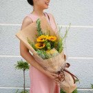 Woman holding a bouquet of sunflowers wrapped in brown paper with a bow.